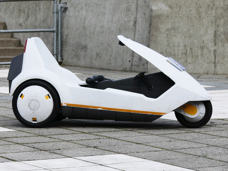 A Sinclair C5 personal vehicle parked near a concrete wall